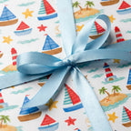 Nautical wrapping paper with watercolor sailboats, tied with a blue satin ribbon by Wrapped Studios.