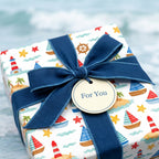 Nautical gift wrap with sailboats, lighthouses, and a navy blue ribbon bow by Wrapped Studios.