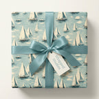 Nautical-themed gift wrapped in sailboat pattern paper with a teal satin ribbon and bow.