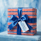 Patriotic red, white, and blue striped wrapping paper with a blue satin bow on a gift box by Wrapped Studios.