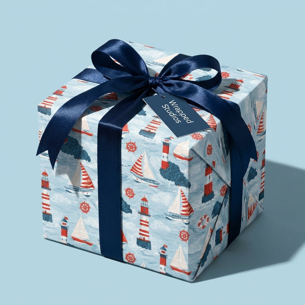 Nautical wrapping paper with sailboats and lighthouses, tied with a navy bow on a gift box by Wrapped Studios.