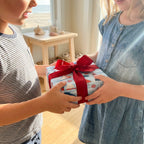 Kids holding a gift in nautical sailboat wrapping paper with a red bow by Wrapped Studios.