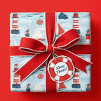 Nautical wrapping paper with lighthouses and sailboats, tied with a red ribbon bow by Wrapped Studios.