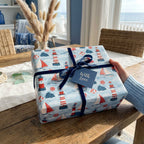 Nautical lighthouse and sailboat wrapping paper with a navy velvet bow by Wrapped Studios.