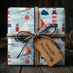 Nautical wrapping paper with red lighthouses and sailboats on a gift box, by Wrapped Studios.