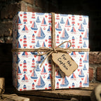Blue and red nautical wrapping paper with sailboats and lighthouses on a gift box by Wrapped Studios.
