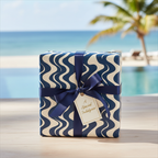 Modern wavy navy blue and cream wrapping paper on a gift box with a navy ribbon, tag, and tropical beach background.