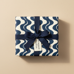 Modern navy blue and cream wave pattern wrapping paper with a dark blue ribbon bow and "Wrapped Studios" gift tag, ideal for elegant gifts.