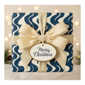 Merry Christmas gift in modern navy blue and white wave wrapping paper, tied with an elegant champagne ribbon and a festive tag.