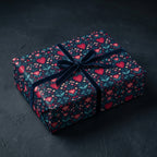 Luxury gift wrap with a romantic pattern of red hearts and floral elements on a dark blue background, tied with a velvet ribbon bow.