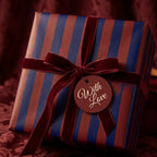 Luxury striped gift wrap in navy and burgundy with a velvet bow and "With Love" tag by Wrapped Studios.