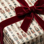 Christmas gift wrap featuring a nutcracker pattern and a burgundy velvet ribbon.