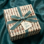 Gift box wrapped in nutcracker-themed Christmas wrapping paper with teal velvet ribbon and "For You" tag.