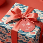 Luxury ocean wave gift wrap in blue and coral with a satin bow and 'With Love' tag by Wrapped Studios.