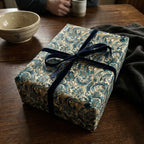 Elegant gift wrapped in teal floral wrapping paper with a navy velvet ribbon on a rustic wooden table.