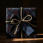 Elegant floral wrapping paper in dark blues and burgundy, tied with black ribbon and twine, featuring a handmade tag.