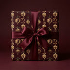 Luxury burgundy Christmas wrapping paper with gold ornament pattern and satin ribbon bow by Wrapped Studios.