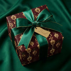 Luxury burgundy and gold Christmas wrapping paper with emerald green bow by Wrapped Studios.