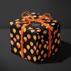 Black birthday wrapping paper with watercolor orange balloons and a raffia bow by Wrapped Studios.