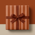 Terracotta striped wrapping paper with a burnt orange ribbon bow on a square gift box, by Wrapped Studios.
