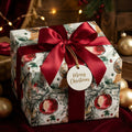 Elegant Christmas gift wrap with watercolor ornaments and red satin bow by Wrapped Studios.