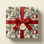 Elegant watercolor Christmas wrapping paper with red ornaments and a red satin bow by Wrapped Studios.