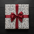 Elegant gift wrapped in vintage floral wrapping paper with a satin burgundy ribbon on a black wood surface.