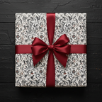 Elegant gift wrapped in vintage floral wrapping paper with a satin burgundy ribbon on a black wood surface.