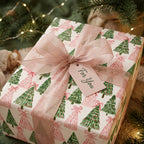 Pink Christmas wrapping paper with watercolor trees and a dusty pink bow by Wrapped Studios.