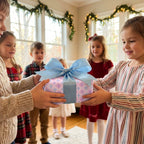 Children holding a gift in pastel cross wrapping paper with a blue bow, by Wrapped Studios.