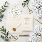 Graduation wrapping paper with watercolor pink and blue caps and matching invitation set by Wrapped Studios.