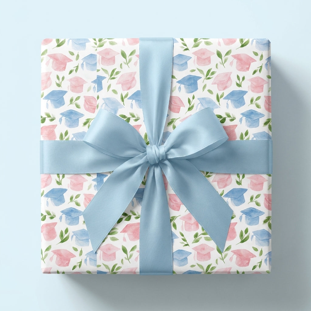 Watercolor graduation wrapping paper with pink and blue caps and a blue bow by Wrapped Studios.