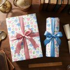 Graduation wrapping paper with pink and blue watercolor mortarboards and satin bows by Wrapped Studios.