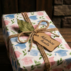 Graduation wrapping paper with pink and blue watercolor caps, rustic twine, and tag by Wrapped Studios.