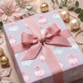 Pastel Christmas wrapping paper with watercolor ornaments and a pink bow by Wrapped Studios.