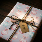 Pastel Christmas wrapping paper with watercolor ornaments, twine, and a Joy tag by Wrapped Studios.