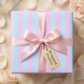 Pastel pink and blue striped baby shower gift wrap with a satin ribbon bow by Wrapped Studios.