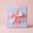 Pastel pink and blue striped wrapping paper with a satin ribbon bow on a gift box by Wrapped Studios.