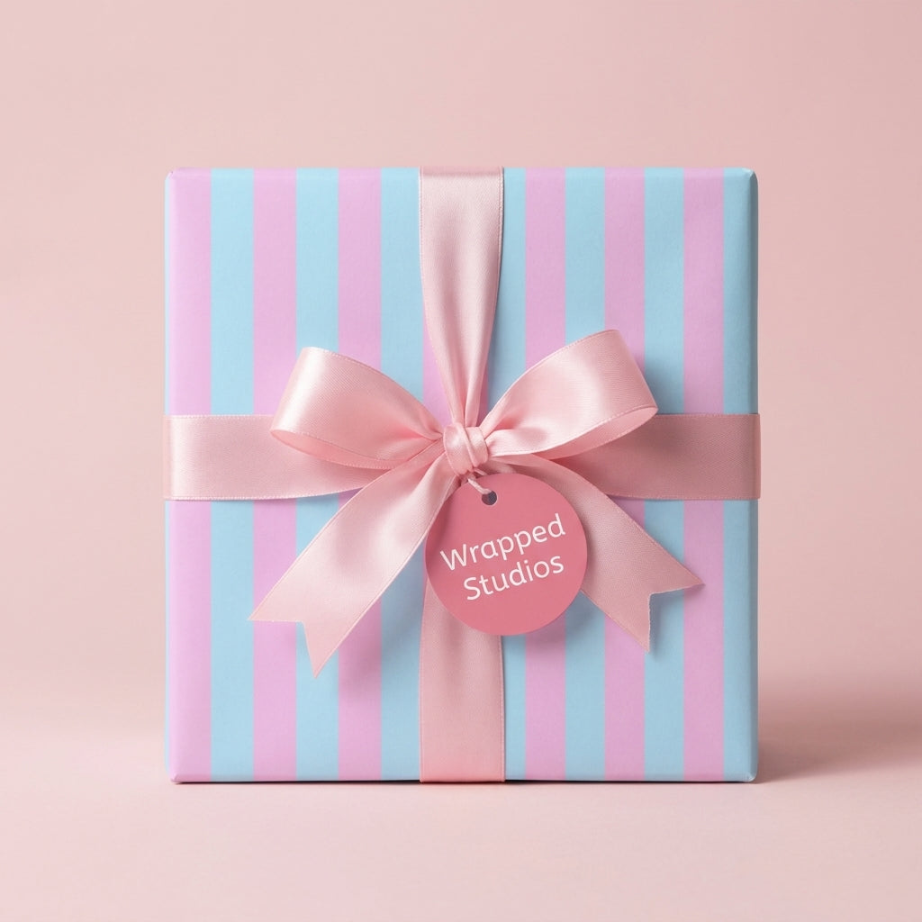 Pastel pink and blue striped wrapping paper with a satin ribbon bow on a gift box by Wrapped Studios.