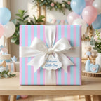 Pink and blue striped baby shower wrapping paper with white bow and Welcome Little One tag by Wrapped Studios.