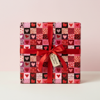 Love hearts patchwork wrapping paper for Valentine's Day or anniversary gifts, tied with a red satin ribbon and "Wrapped Studios" tag.
