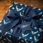 US Air Force wrapping paper in navy blue with stars, fabric ribbon, and "Hero" tag by Wrapped Studios.