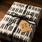 Piano keys wrapping paper for music lovers with black twine and For Him gift tag by Wrapped Studios.