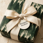 Green pine forest wrapping paper with a cream ribbon and Wrapped Studios gift tag for rustic holiday gift wrap.