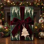 Luxury forest Christmas wrapping paper with a burgundy velvet bow and wooden tree tag by Wrapped Studios.