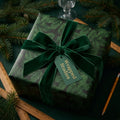 Luxury Christmas wrapping paper with green pine needle pattern, velvet bow, and tag by Wrapped Studios.