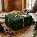 Green pine Christmas wrapping paper with gold ribbon on a rustic holiday gift box by Wrapped Studios.