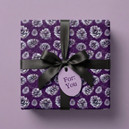 Luxury Christmas gift wrap. Purple paper with pine cone pattern tied with a black satin ribbon and gift tag.