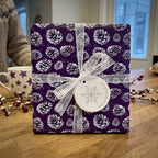 Elegant purple Christmas gift wrap with pine cone pattern and lace ribbon.