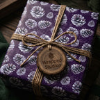 Elegant purple Christmas gift wrap with pinecone pattern and rustic twine bow by Wrapped Studios.